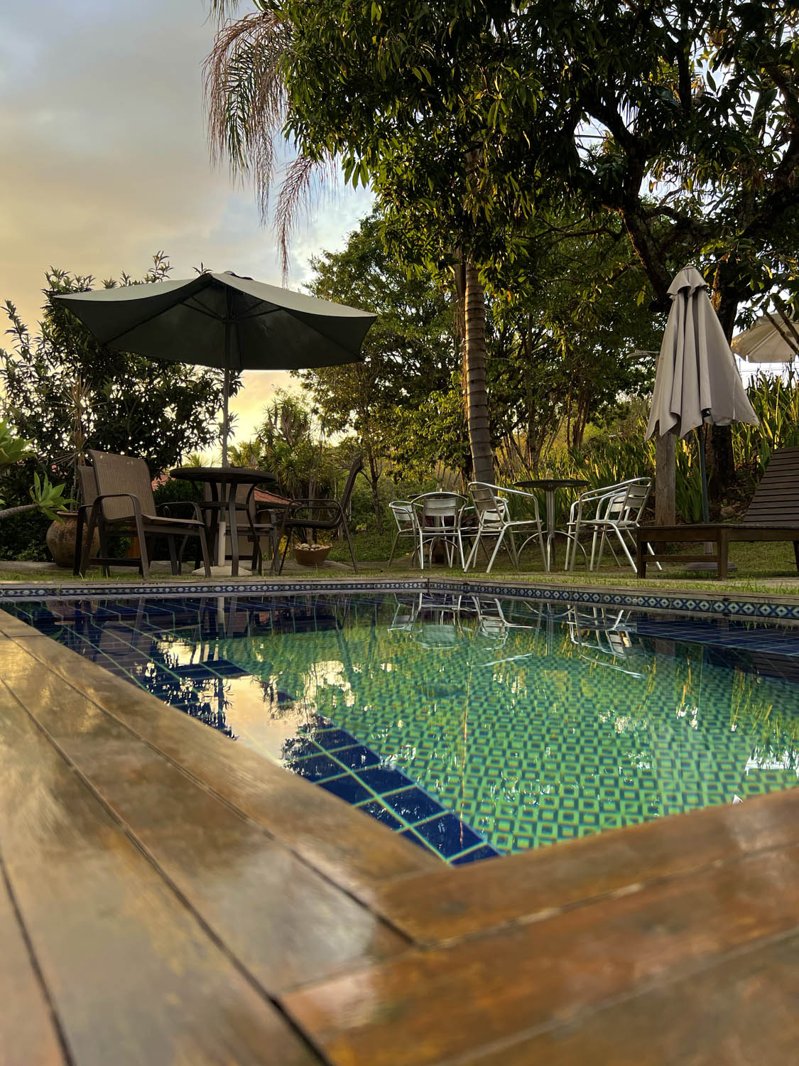 Piscina da pousada ao entardecer cercada por jardim e árvores